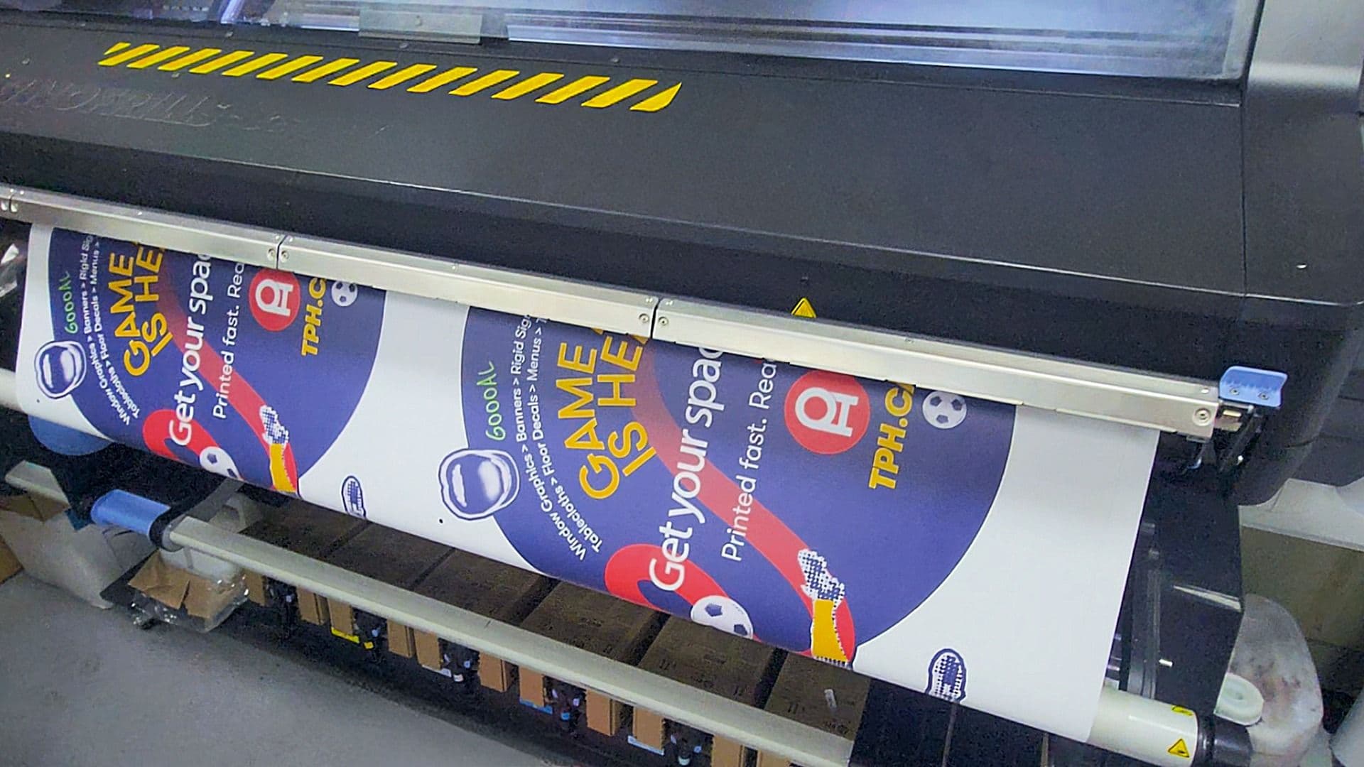 A large format printer producing a custom Easy Dot window decal for a retail storefront promotion featuring a bold blue design and football tournament messaging.