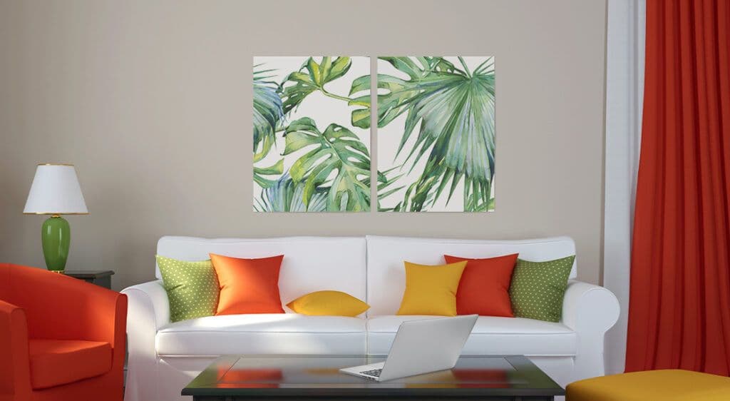 Two large posters hang side by side above a living room couch with a laptop on a coffee table in the foreground. Posters feature oversize green tropical foliage on a white background.
