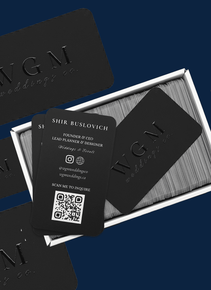 Stack of premium black business cards with rounded corners and embossed Spot UV logo reading “WGM wedding co.”, displayed in an open box with two cards showing contact details and a QR code.