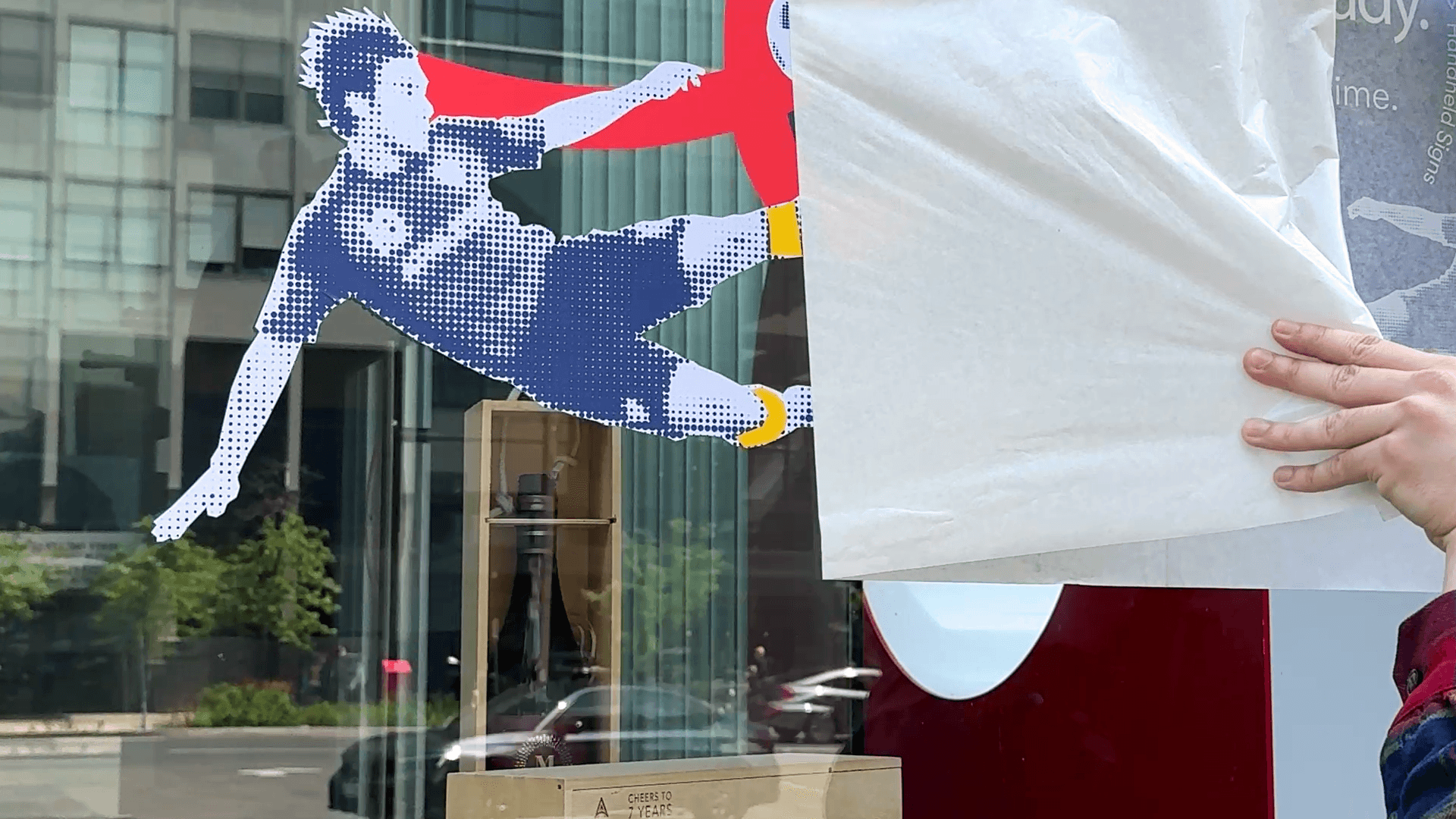 Hand peeling a film from a window graphic of a blue and white soccer player kicking.