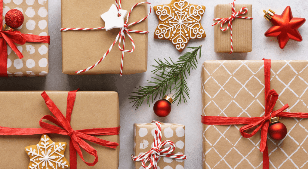 Array of wrapped Christmas gifts of various shapes and sizes, decorated with red ribbon and gingerbread cookie decor