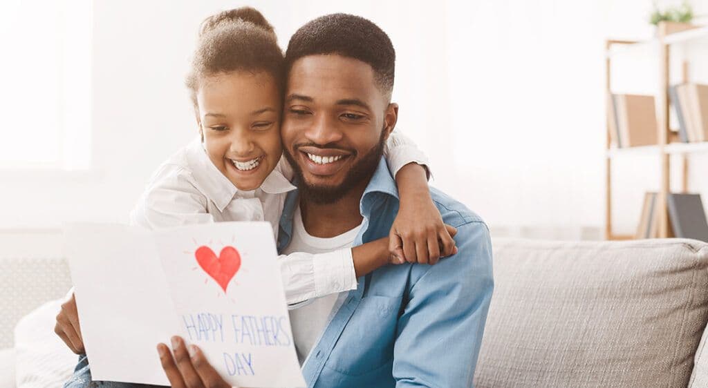 father and daughter hugging while father holds a home-made card