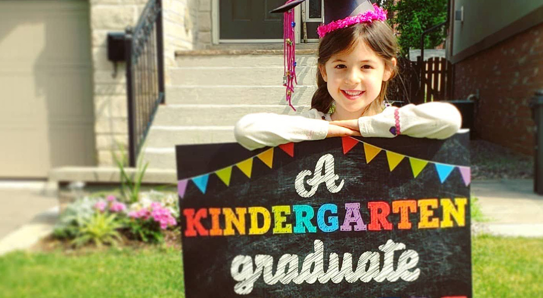 Photo of a smiling girl holding a sign saying "a kindergarten graduate".